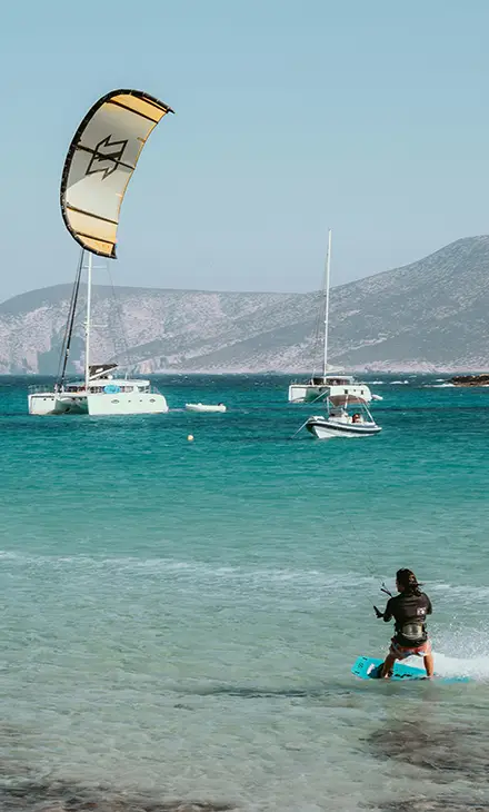 Person holding on the the kite handle while surfing and three boats in the background