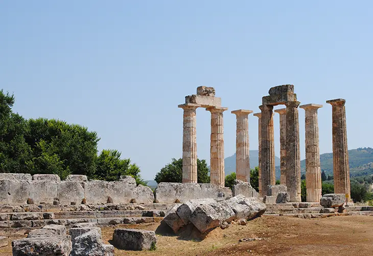 Nine standing, pillars of the temple of Zeus in Nemea, surrounded be stone parts of the ruins